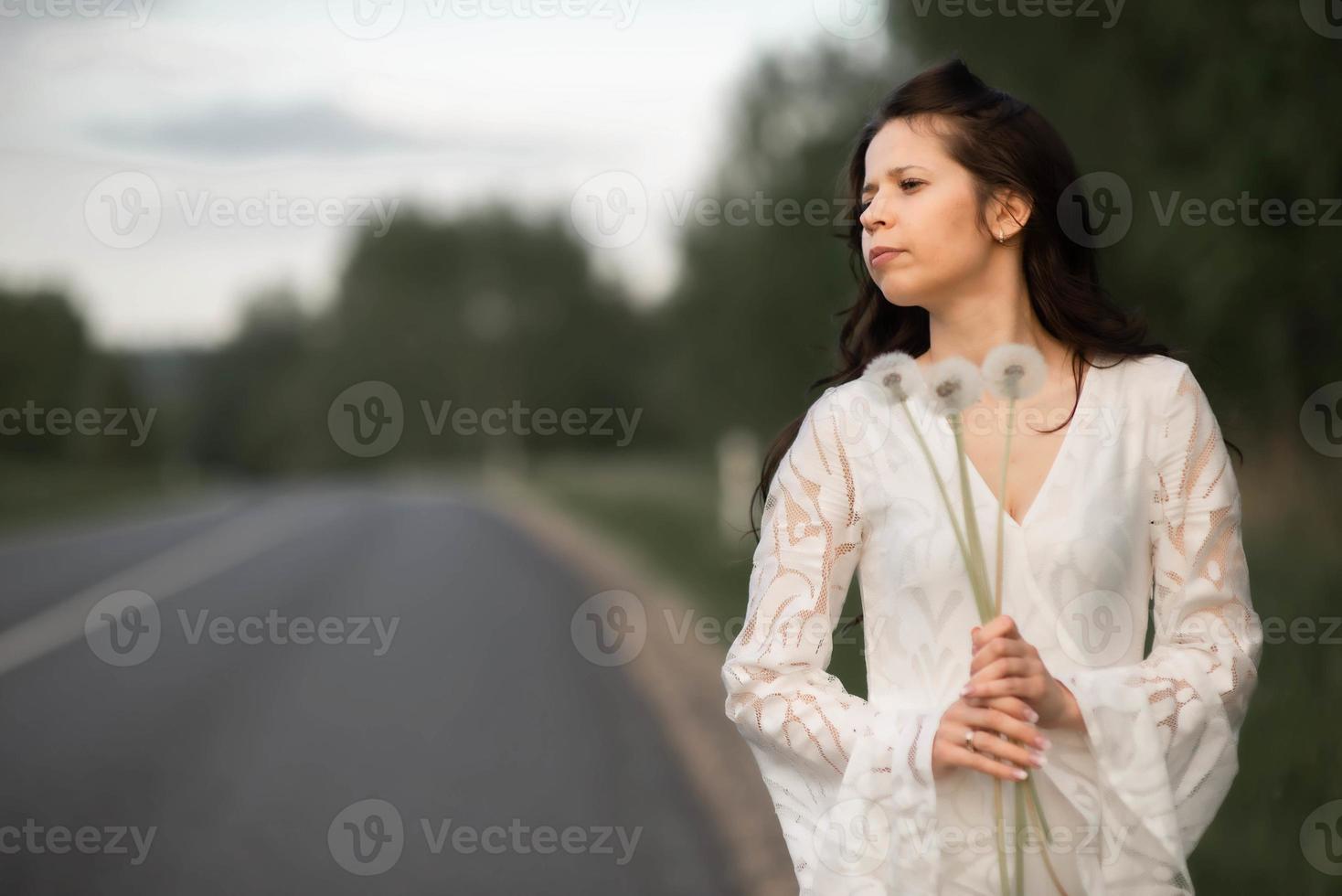 Portrait de jeune femme brune avec pissenlit sur route asphaltée rurale photo