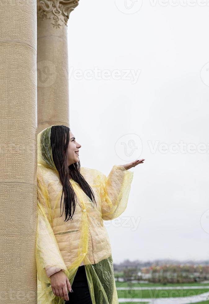 Belle femme brune en imperméable jaune attraper la pluie à l'extérieur photo