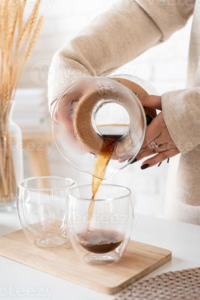 Jeune femme prépare du café dans une cafetière, verse du café dans le verre photo