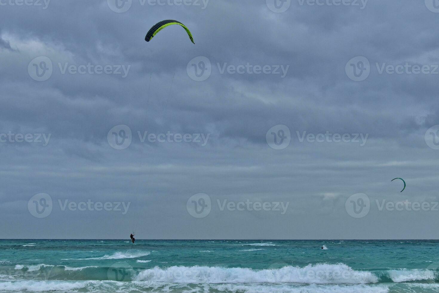 été paysage avec le océan avec foncé nuageux vagues et surfeurmi trousse avec parachutes flottant sur le rive photo