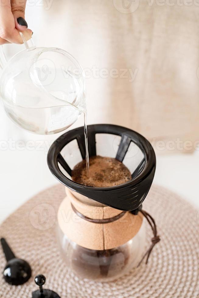femme prépare du café dans une cafetière, verse de l'eau chaude dans le filtre photo