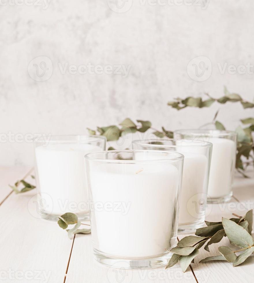 bougies blanches avec des feuilles d'eucalyptus sur fond de bois blanc photo