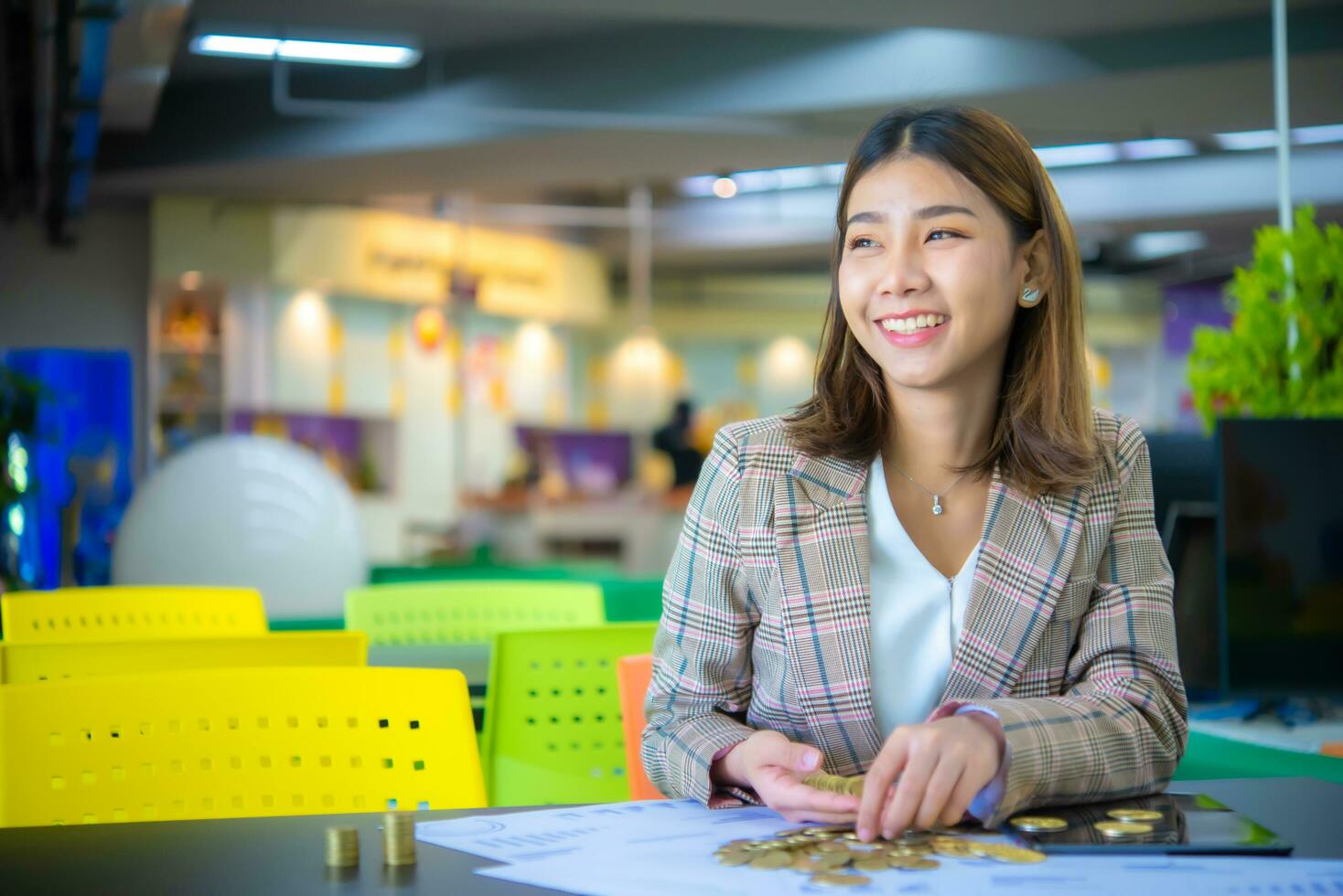 content magnifique asiatique affaires femme en portant une empiler de or pièces de monnaie mis sur une noir table tandis que à la recherche à le copie espace avec sourire sur sa affronter. photo