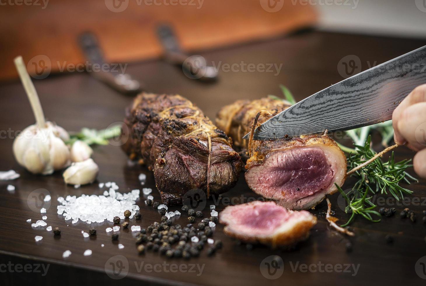 Trancher une portion de rouleau de rosbif biologique avec un couteau sur une table en bois avec du poivre à l'ail et du sel à Melbourne en Australie photo