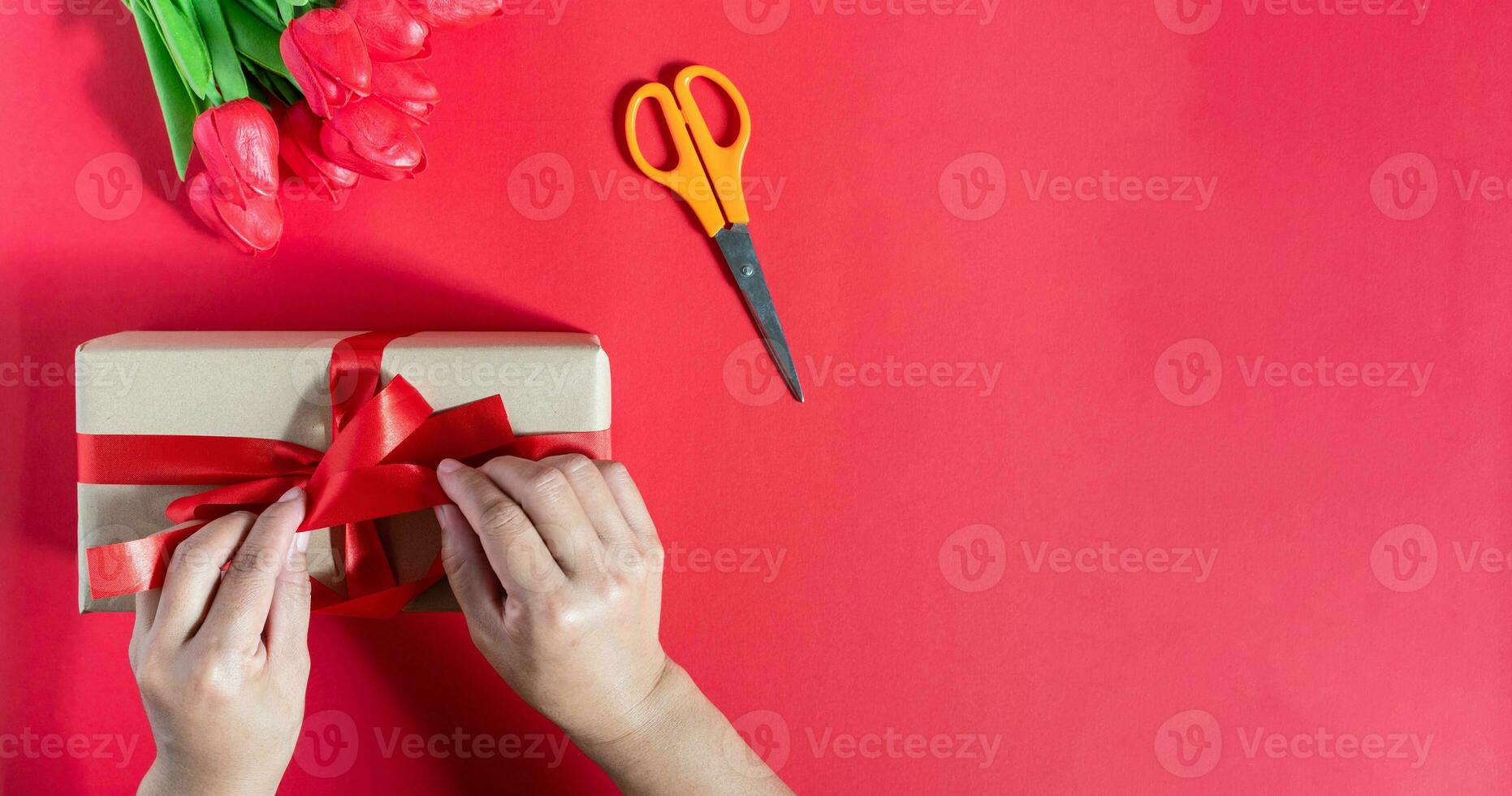 une femme emballage cadeau des boites et lié avec rouge rubans sur une rouge Contexte. le concept pour Valentin jour, Noël, faire la fête, anniversaire. a copie espace sur droite pour conception ou texte. sélectif se concentrer. photo