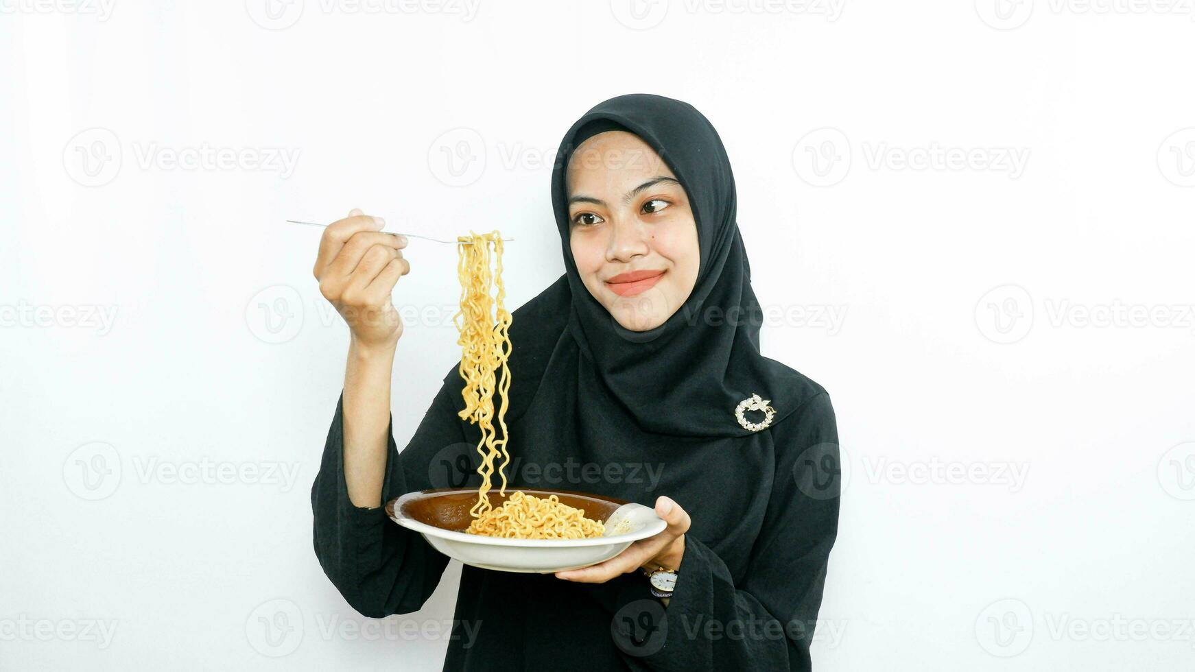 Jeune asiatique femme isolé sur blanc Contexte en portant une assiette de nouilles avec fourchette et en mangeant il photo