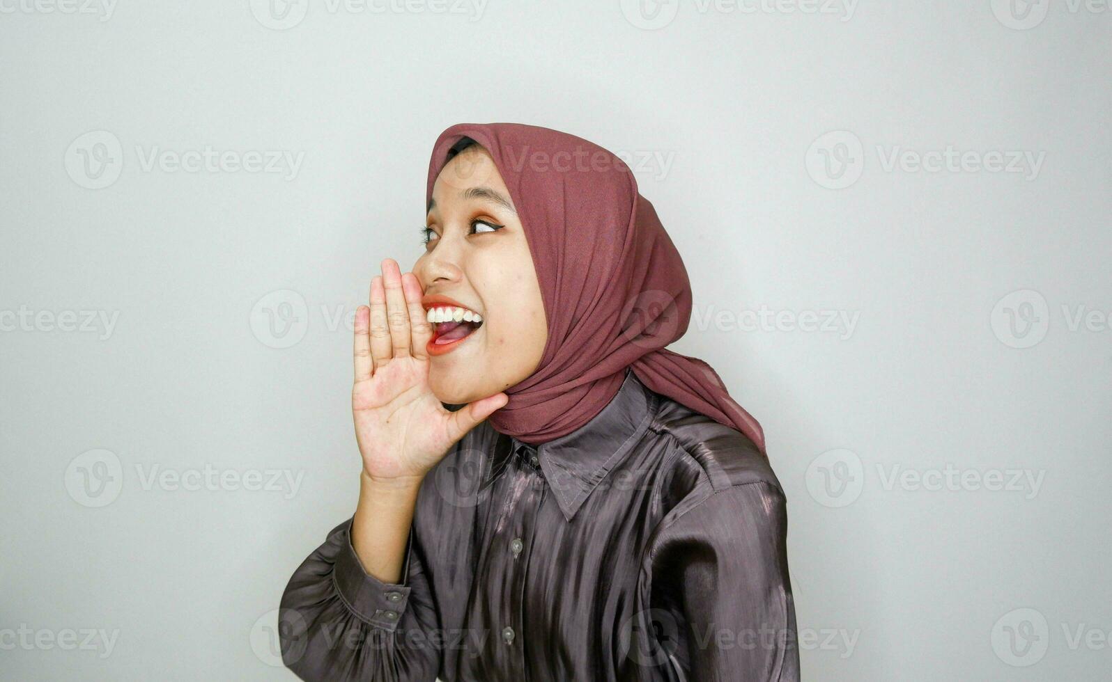 Jeune magnifique asiatique musulman femme portant une foulard en criant et en hurlant bruyant avec une main sur sa bouche. la communication concept. photo