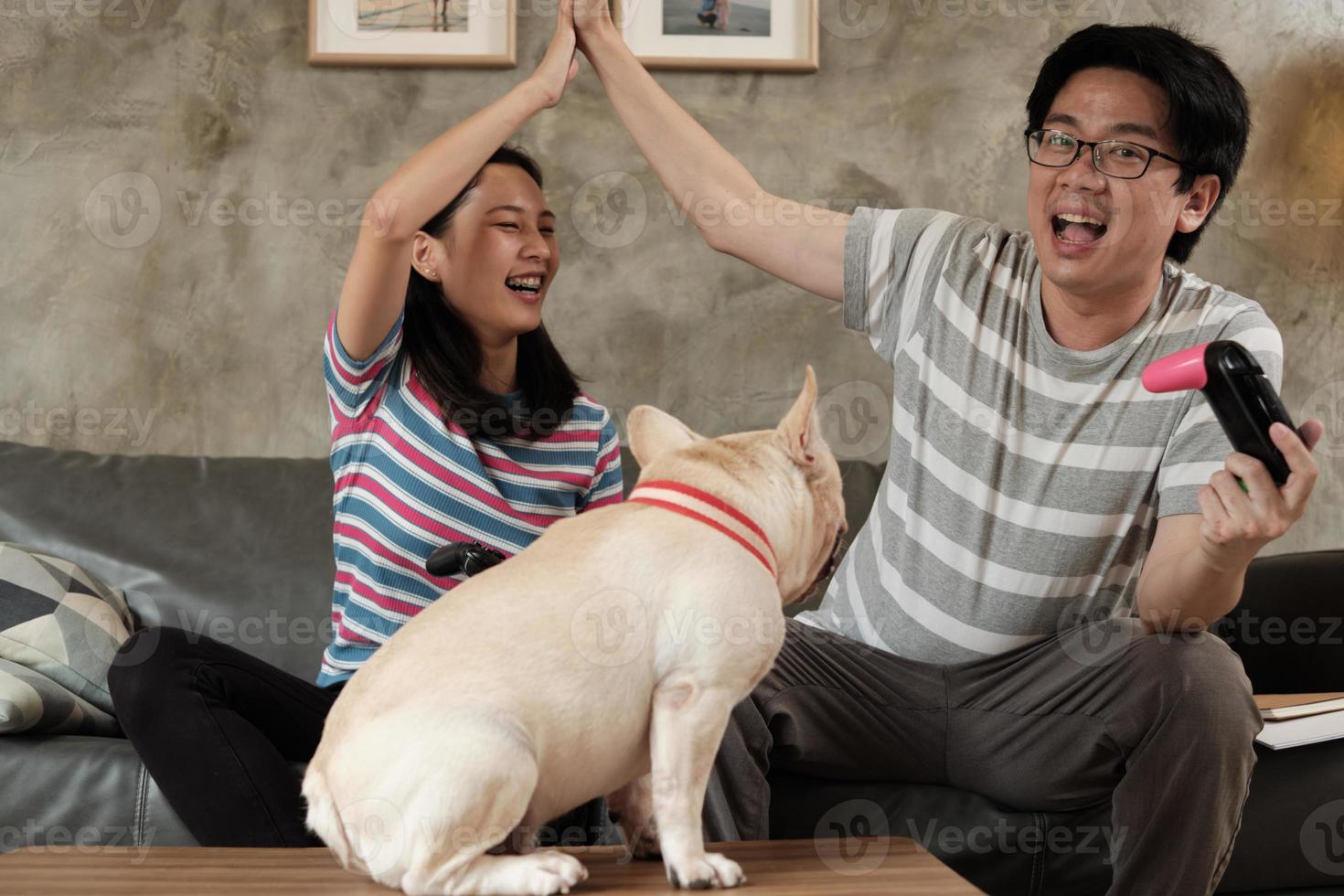 un couple asiatique joue à des jeux vidéo et à un chien de compagnie à proximité. photo