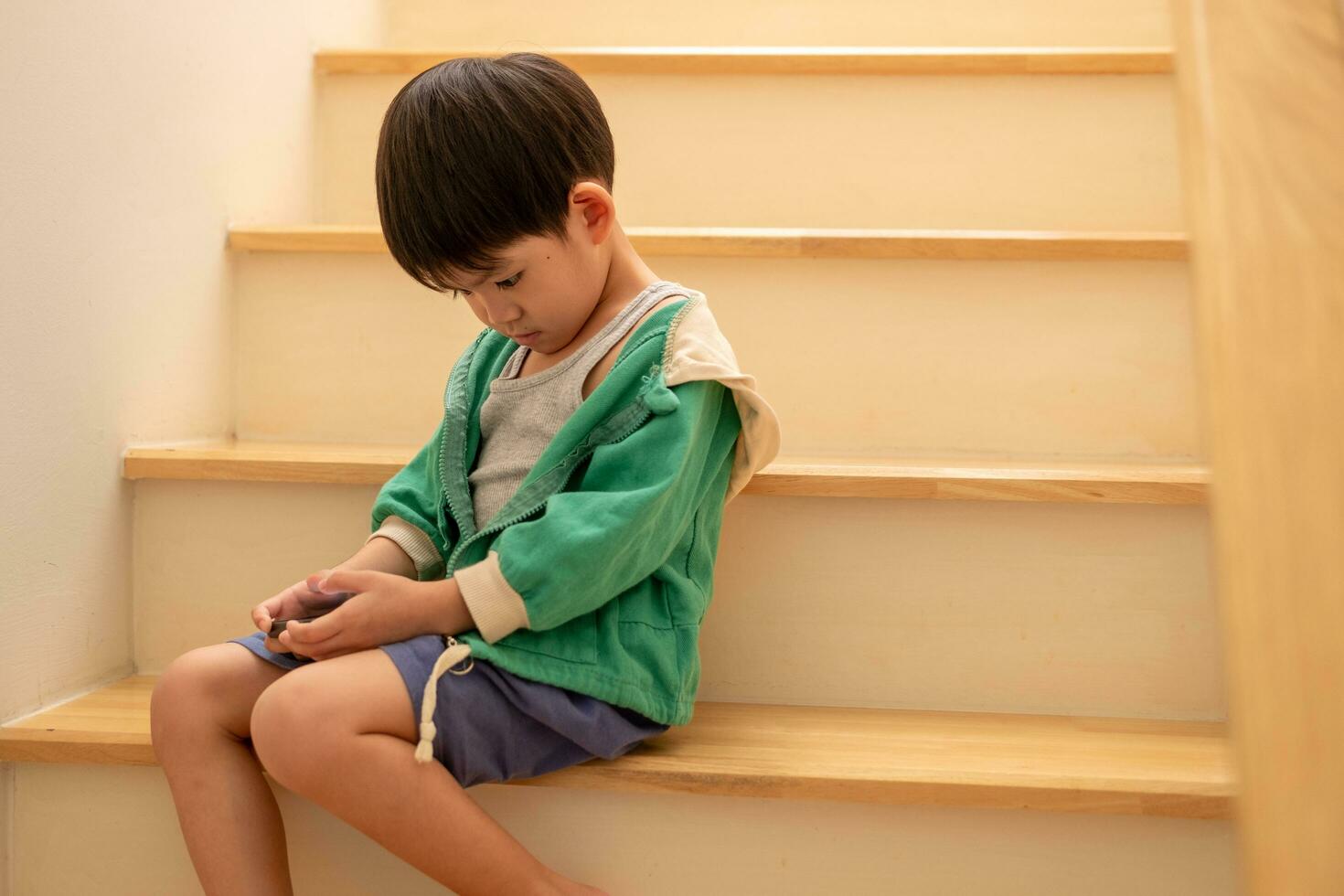 une garçon qui a été grondé par le sien mère secrètement venu à jouer sur le téléphone sur le escaliers. photo