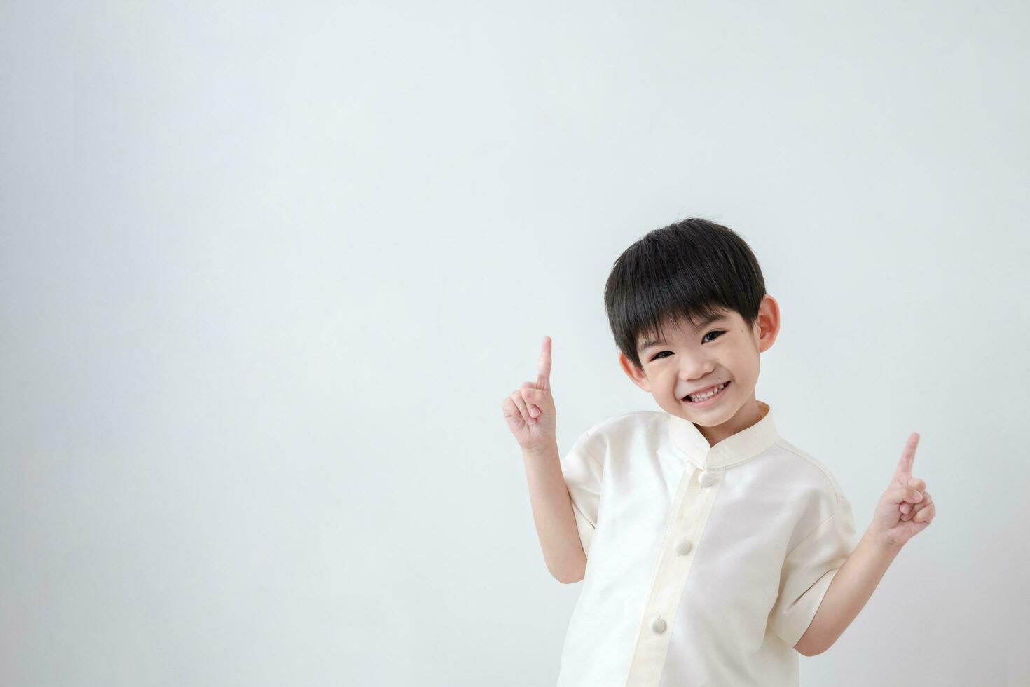 asiatique garçon portant traditionnel thaïlandais vêtements, permanent avec indice doigt vers le haut. sur une blanc Contexte photo