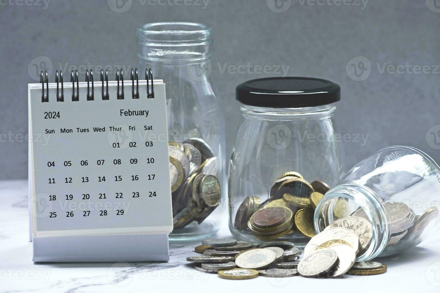 février 2024 calendrier et verre pots avec multi-devise pièces de monnaie. photo