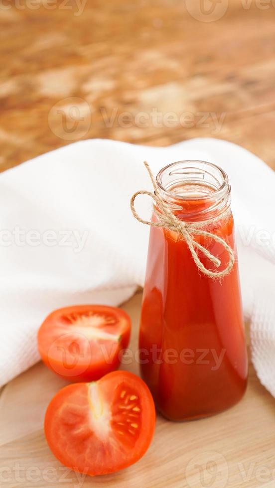 jus de tomate en bouteille de verre et tomates fraîches sur fond de bois photo