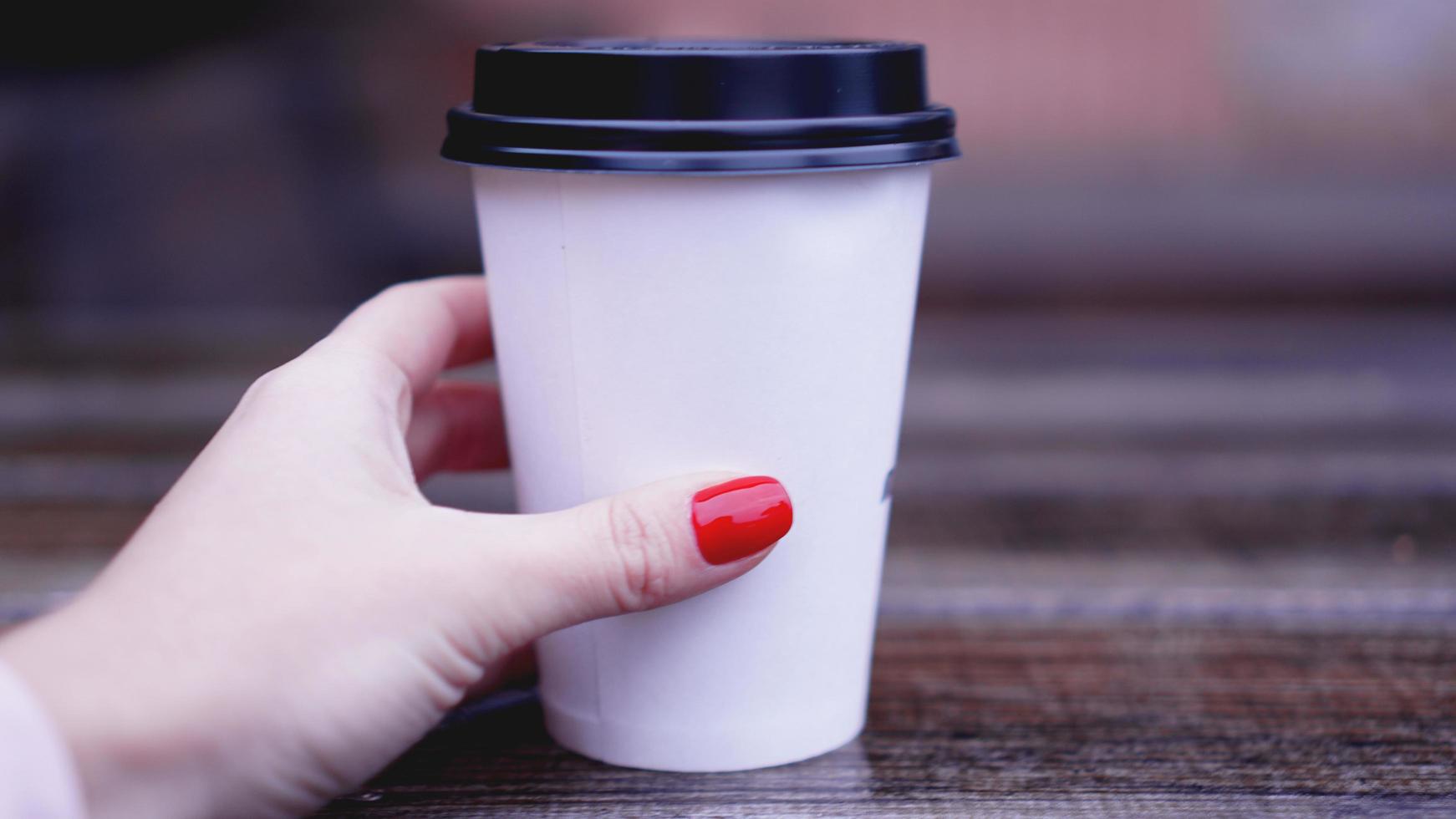 tasse de café sur une table en bois dans des mains féminines. bouchon en plastique de gobelet en papier photo