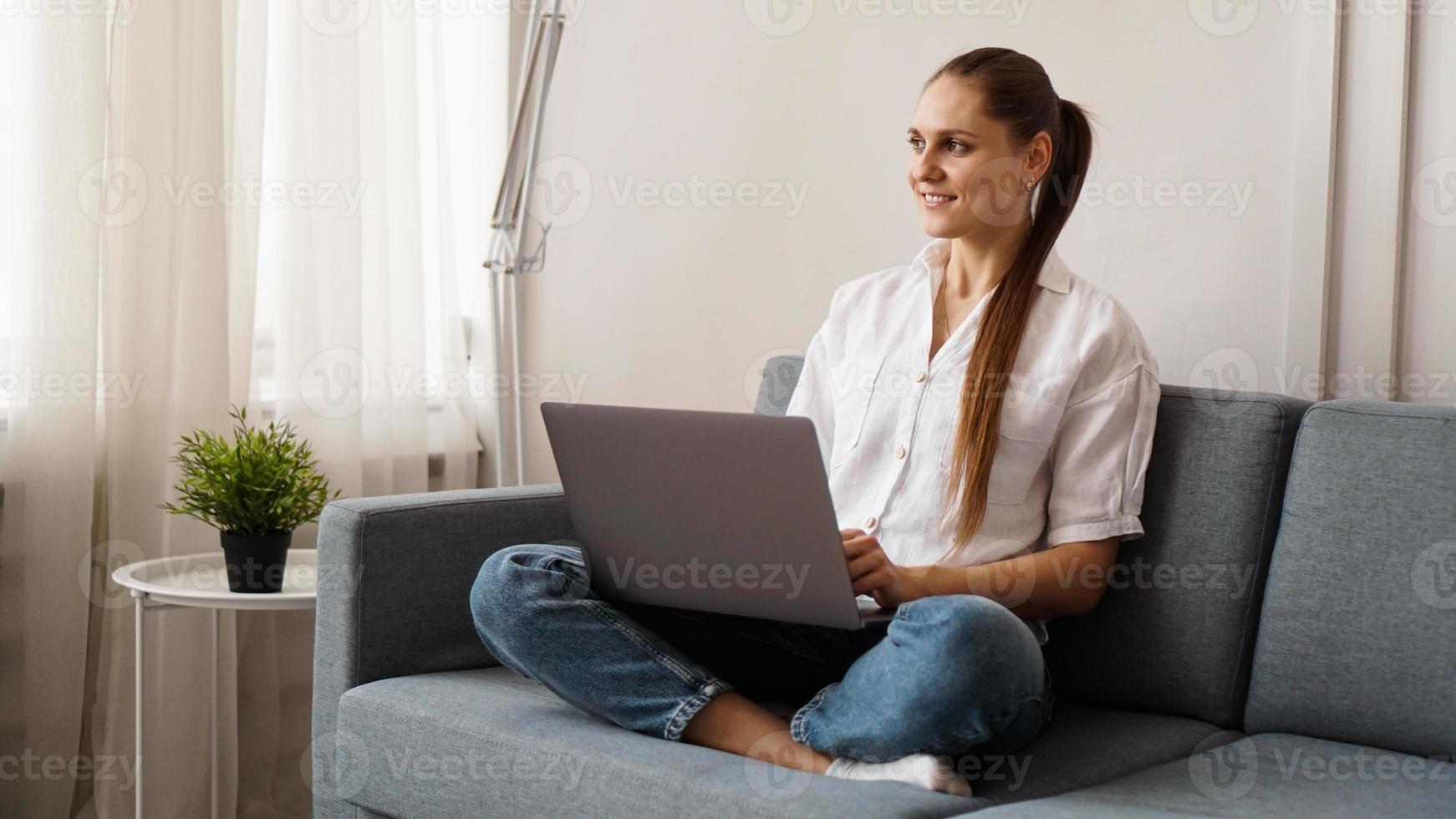 femme heureuse souriante assise sur le canapé et utilisant un ordinateur portable photo