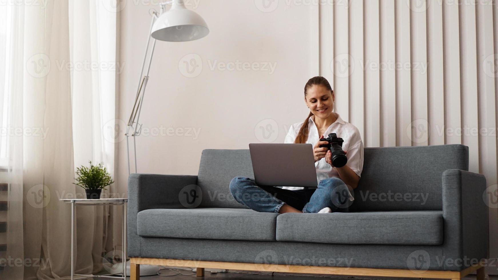 Happy young woman with photo camera using laptop at home