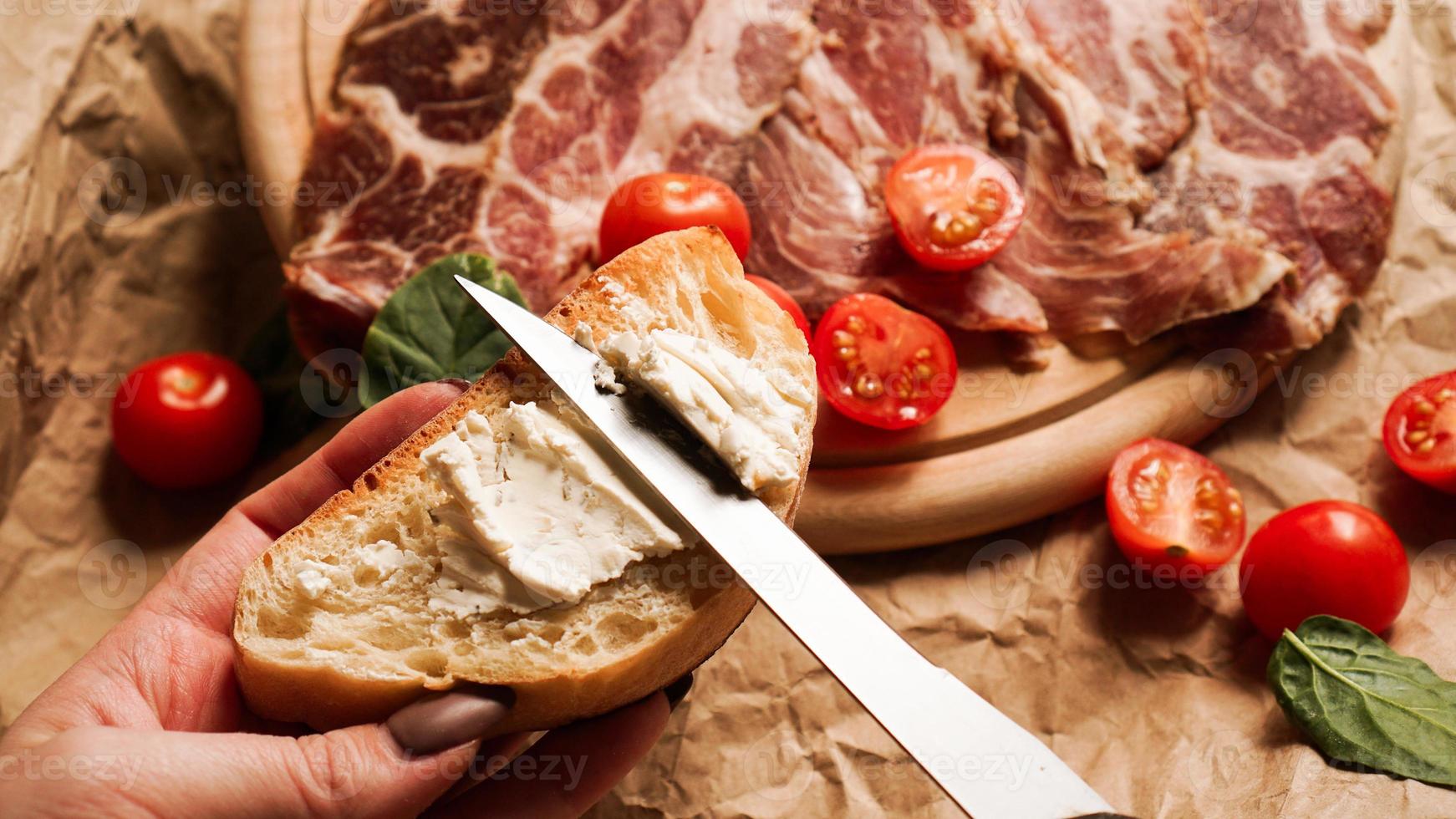 la main d'une femme tient une bruschetta et étale du fromage blanc avec un couteau photo