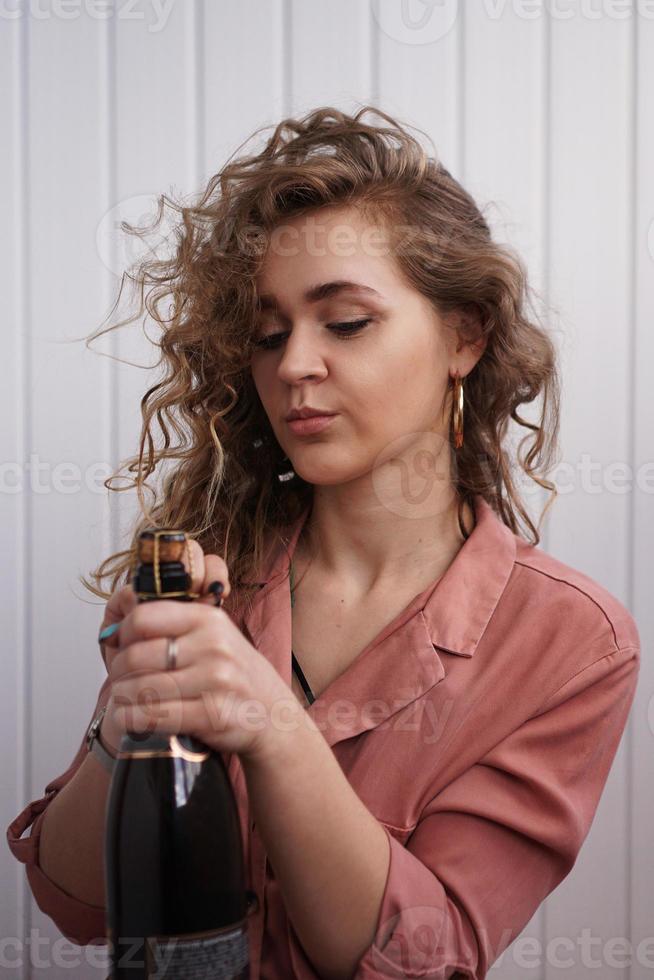 une jeune femme aux cheveux bouclés ouvre une bouteille de champagne photo