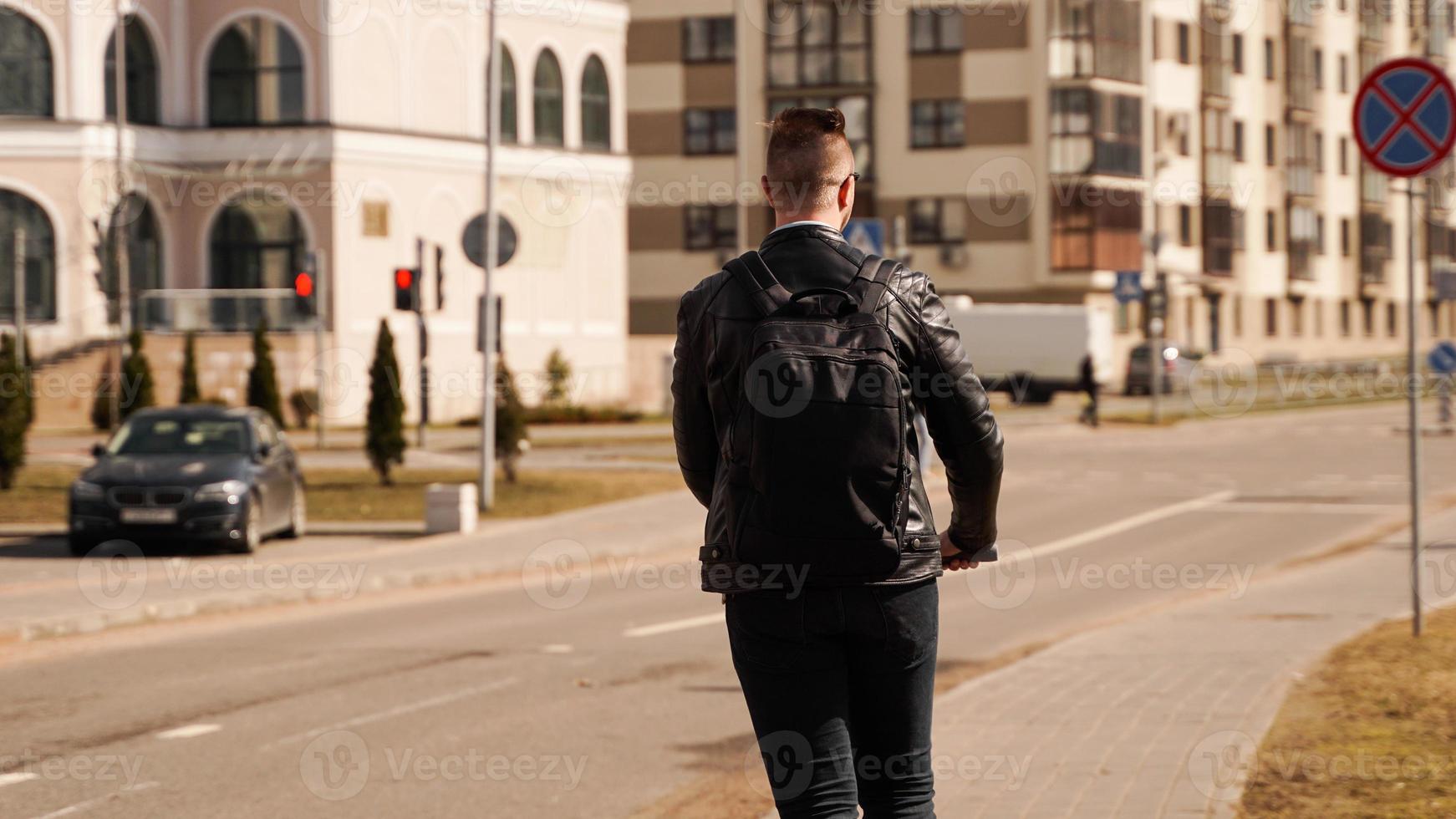 dos d'un homme avec un sac à dos noir. un homme conduit un scooter électrique photo