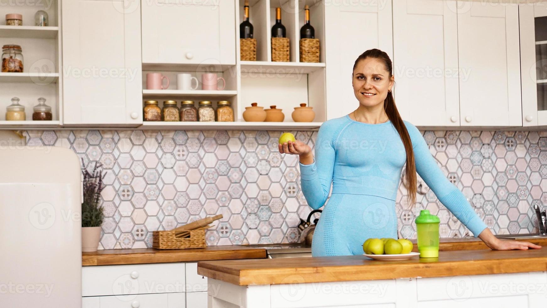 une belle femme dans la cuisine, souriante et tenant une pomme verte photo