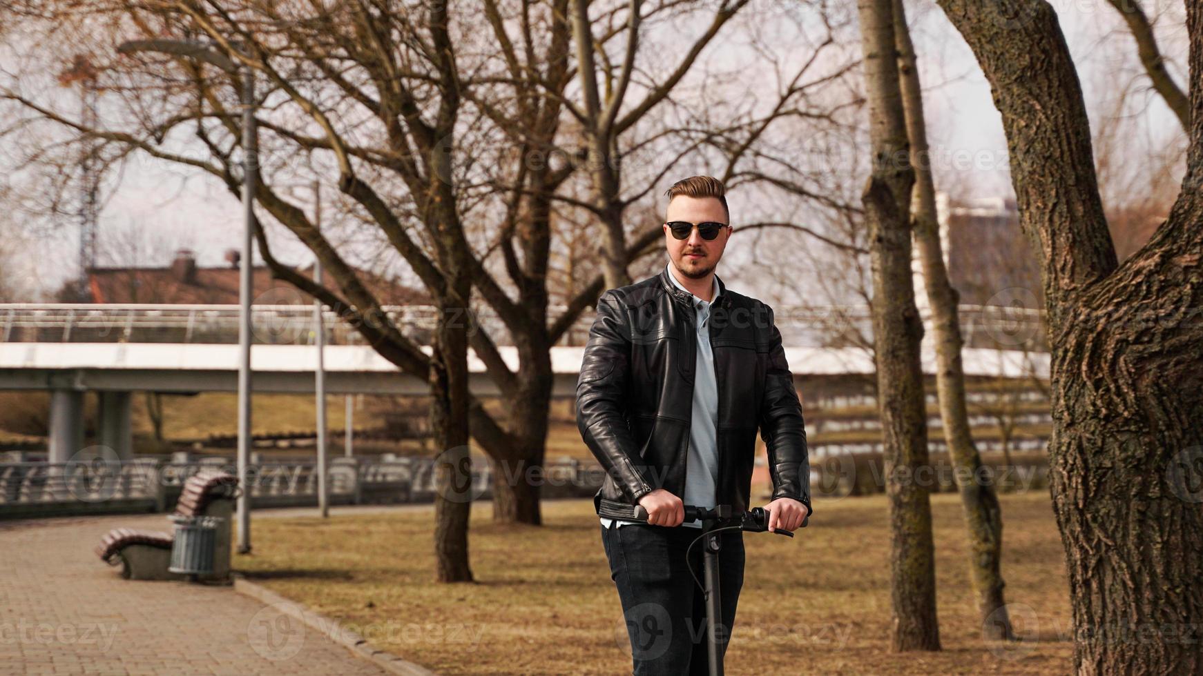 jeune homme dans une veste noire et des lunettes de soleil monte un scooter électronique photo