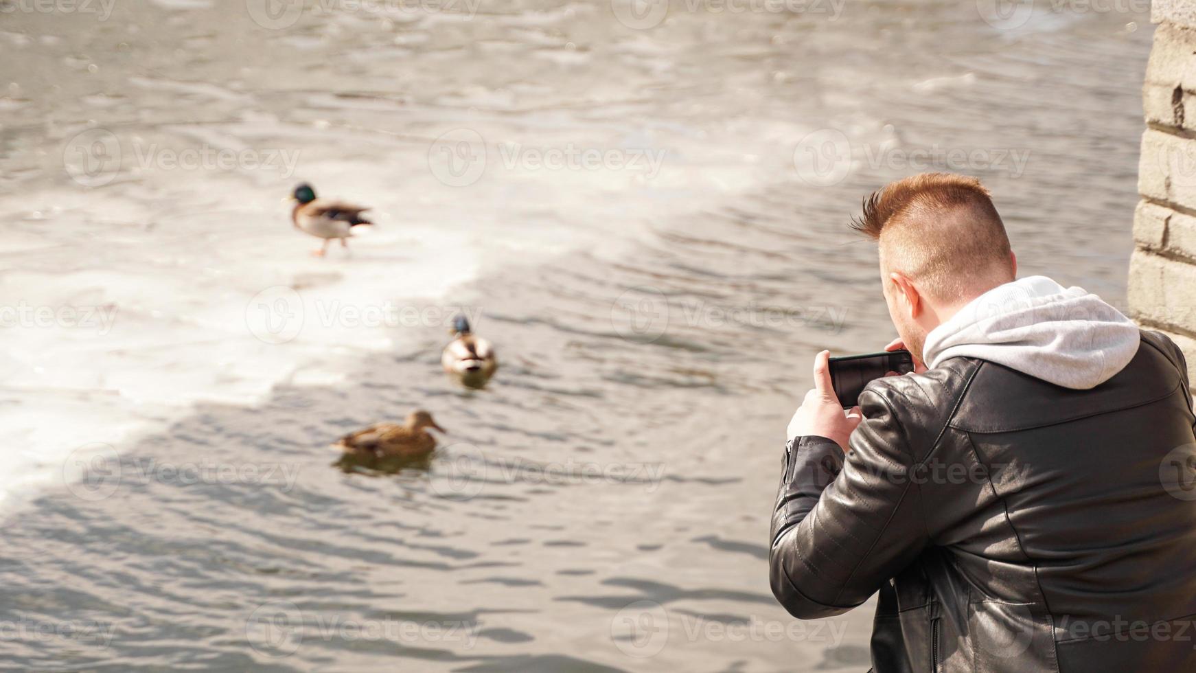 un jeune homme prend des photos de canards sur l'eau. vue de dos.