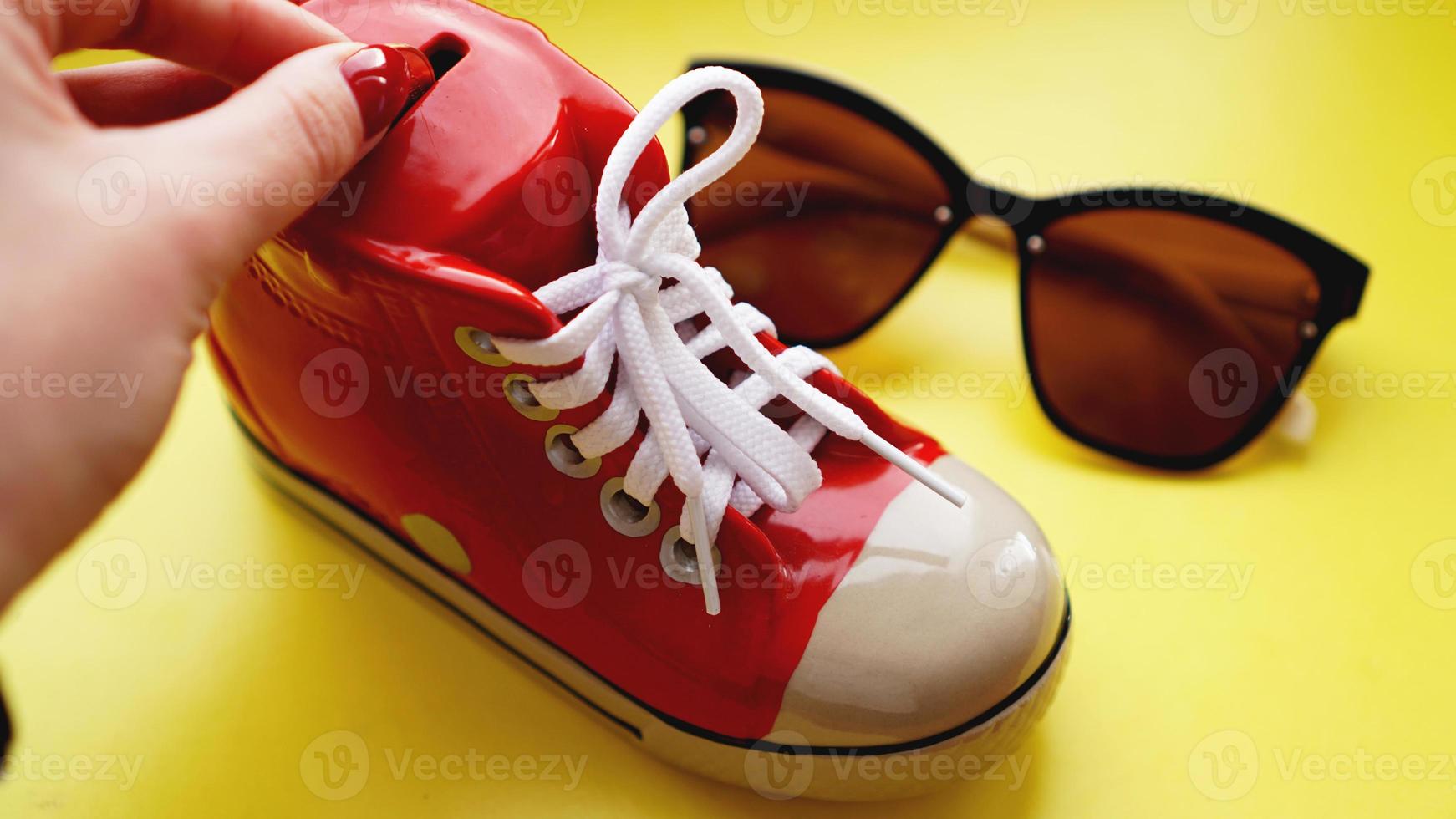 tirelire en forme de baskets. lunettes de soleil sur fond jaune photo