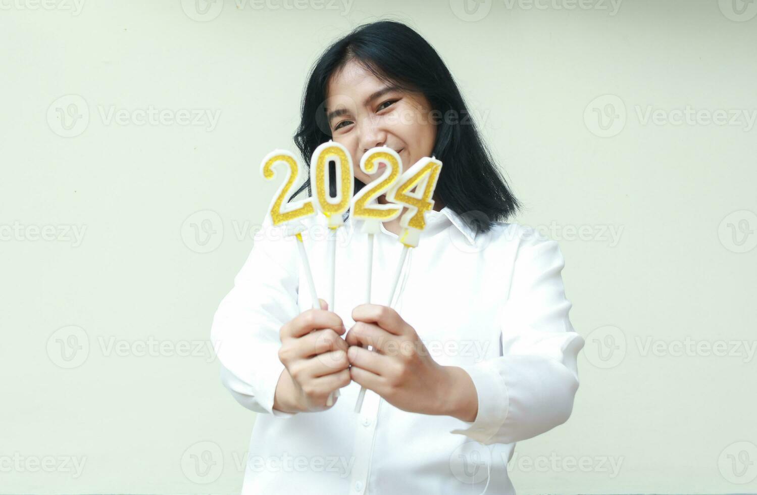 réussi content asiatique femelle Bureau ouvrier souriant à caméra avec excitation par couvrant sa visage avec 2024 d'or bougies Nombres porter blanc chemise formel isolé photo