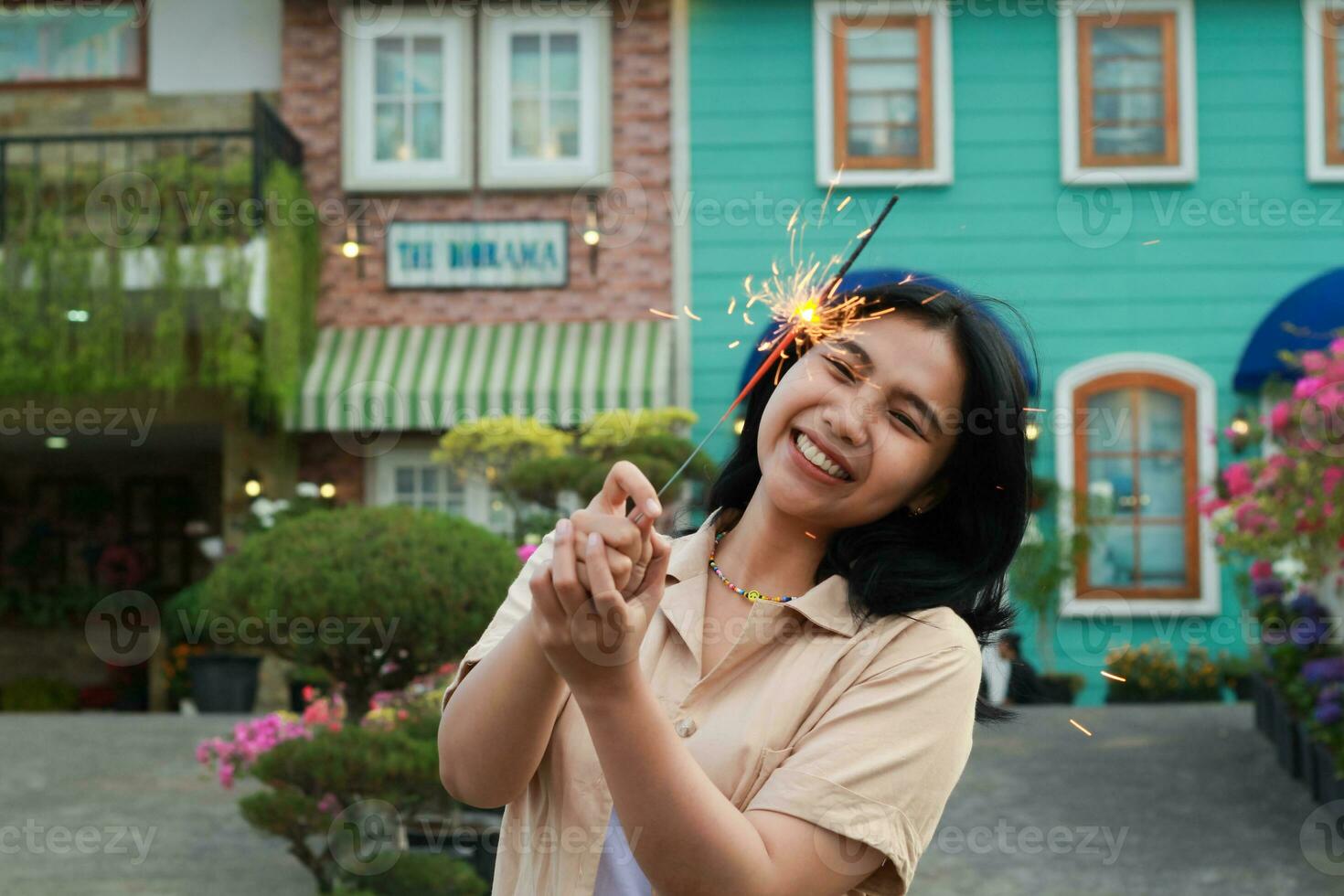 Nouveau année veille fête concept. attrayant asiatique Jeune femme en portant cierge magique avec en riant content dans Extérieur jardin de ancien maison Cour photo