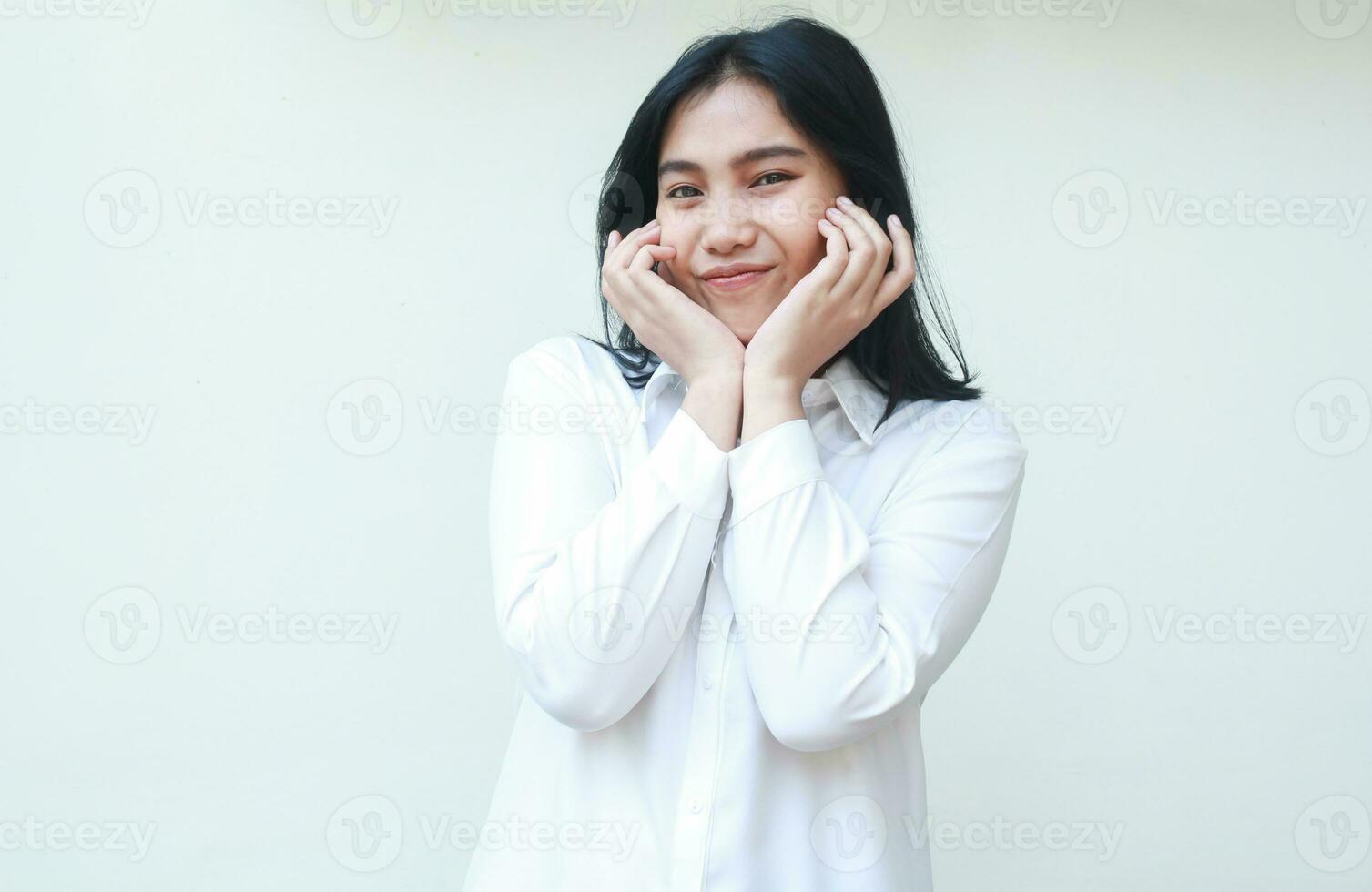 portrait de féminin asiatique femme patron souriant à caméra avec élevage paumes sur menton et les doigts sur joue portant blanc costume chemise permanent plus de isolé Contexte photo