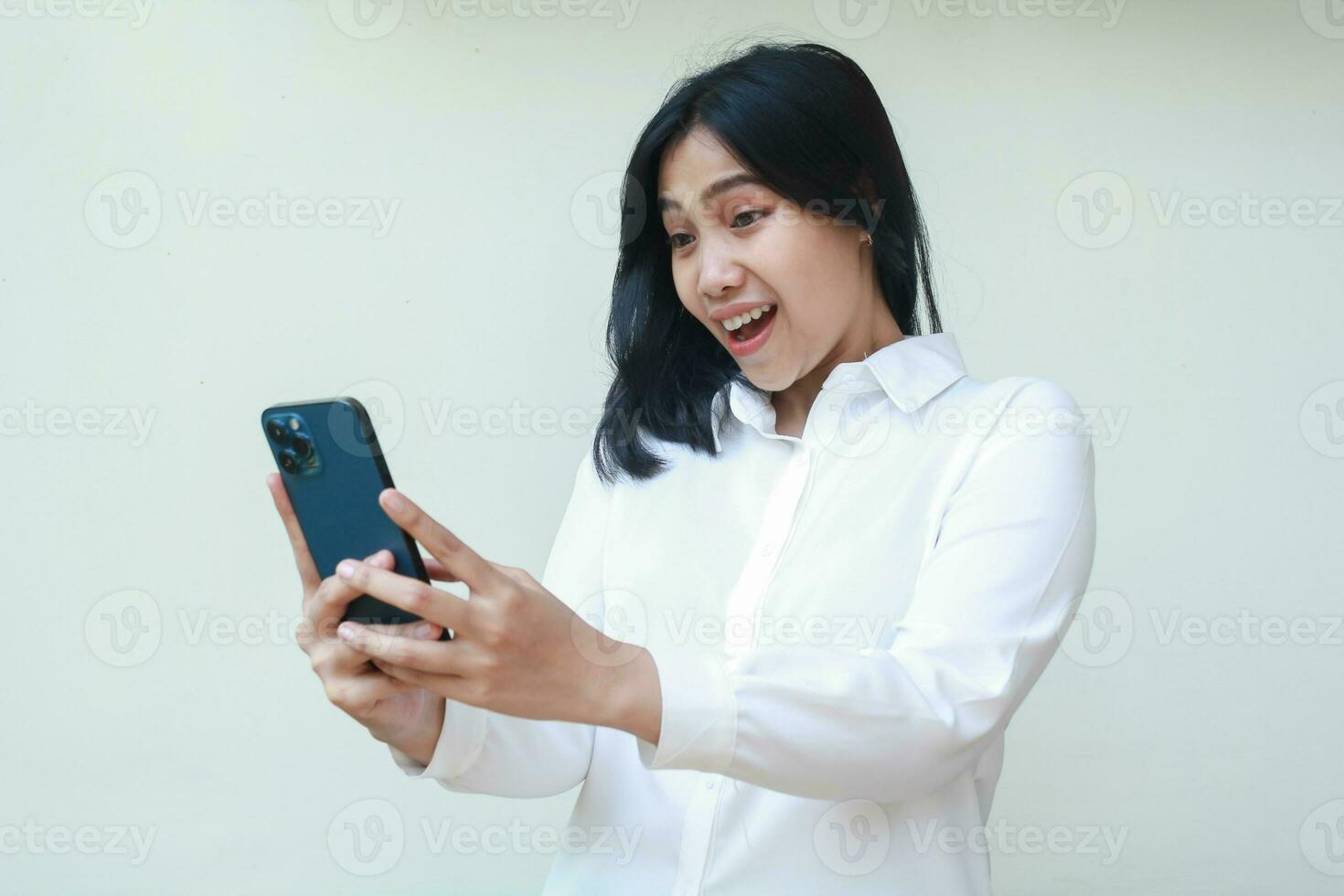 portrait de content asiatique femme sous le choc à la recherche téléphone intelligent tenir sur mains, souriant excité Feuilleter social médias, portant blanc chemise formel costume, lis bien nouvelles de Ventes promotion, permanent isolé photo