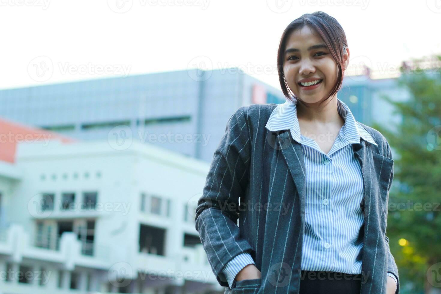 portrait de sur de soi asiatique affaires femme permanent dans en plein air ville rue portant formel gris veste et bleu Bande chemise avec Urbain bulding arrière-plan, femelle financier directeur en marchant dans à l'extérieur photo