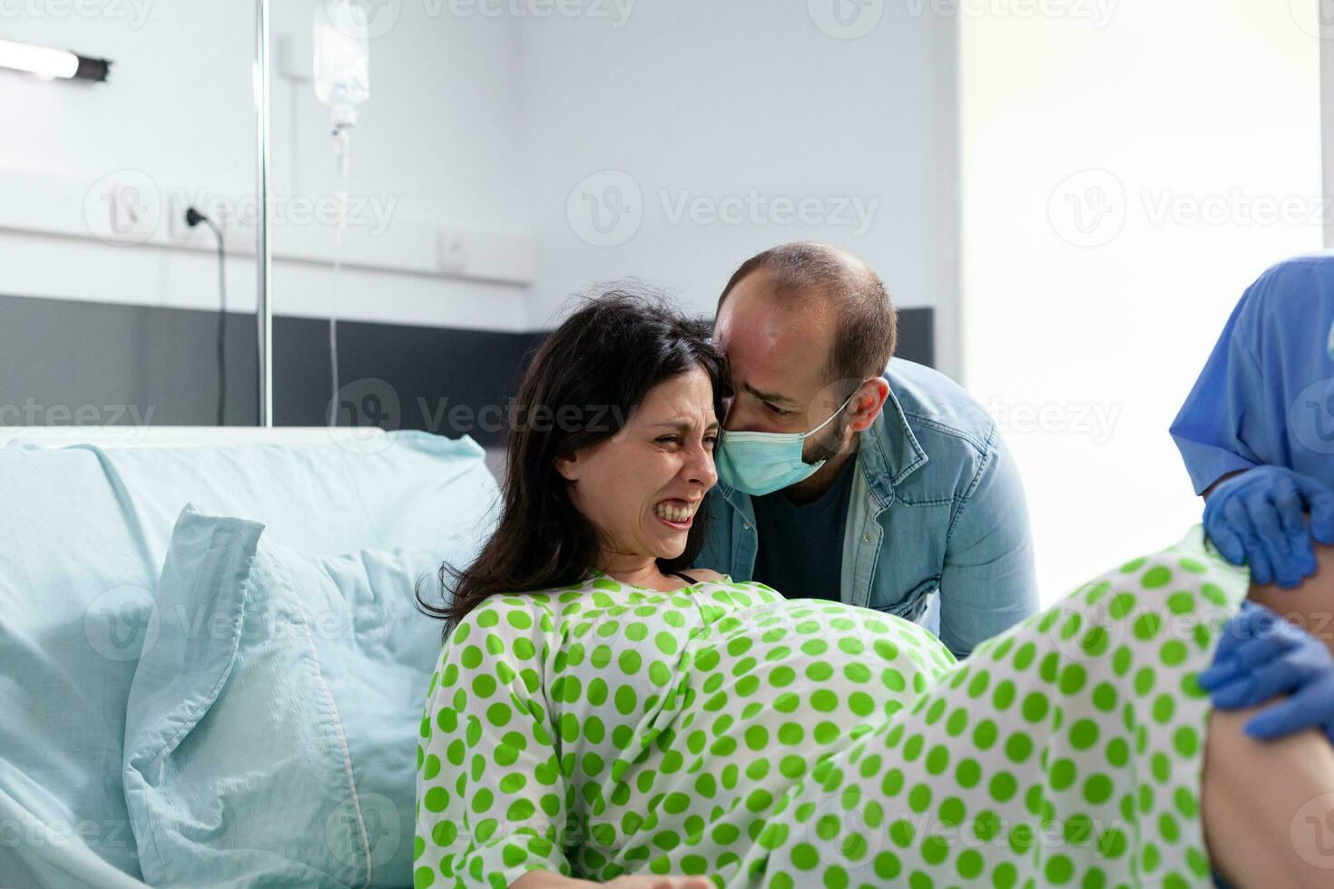 diverse médical équipe portion femme avec grossesse à livraison bébé dans hôpital salle. Enceinte patient ayant douloureux contractions étant réconfortant par mari tandis que donnant naissance à enfant photo