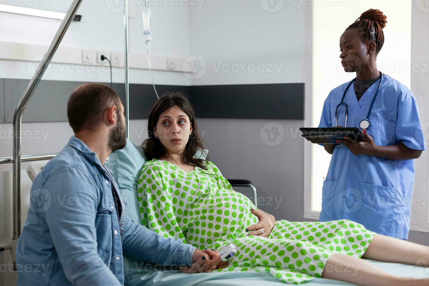 futur Parents discuter avec médical assistant dans hôpital salle, Enceinte femme mensonge dans lit ayant contractions. africain américain infirmière en train de préparer patient avec grossesse pour chirurgie photo