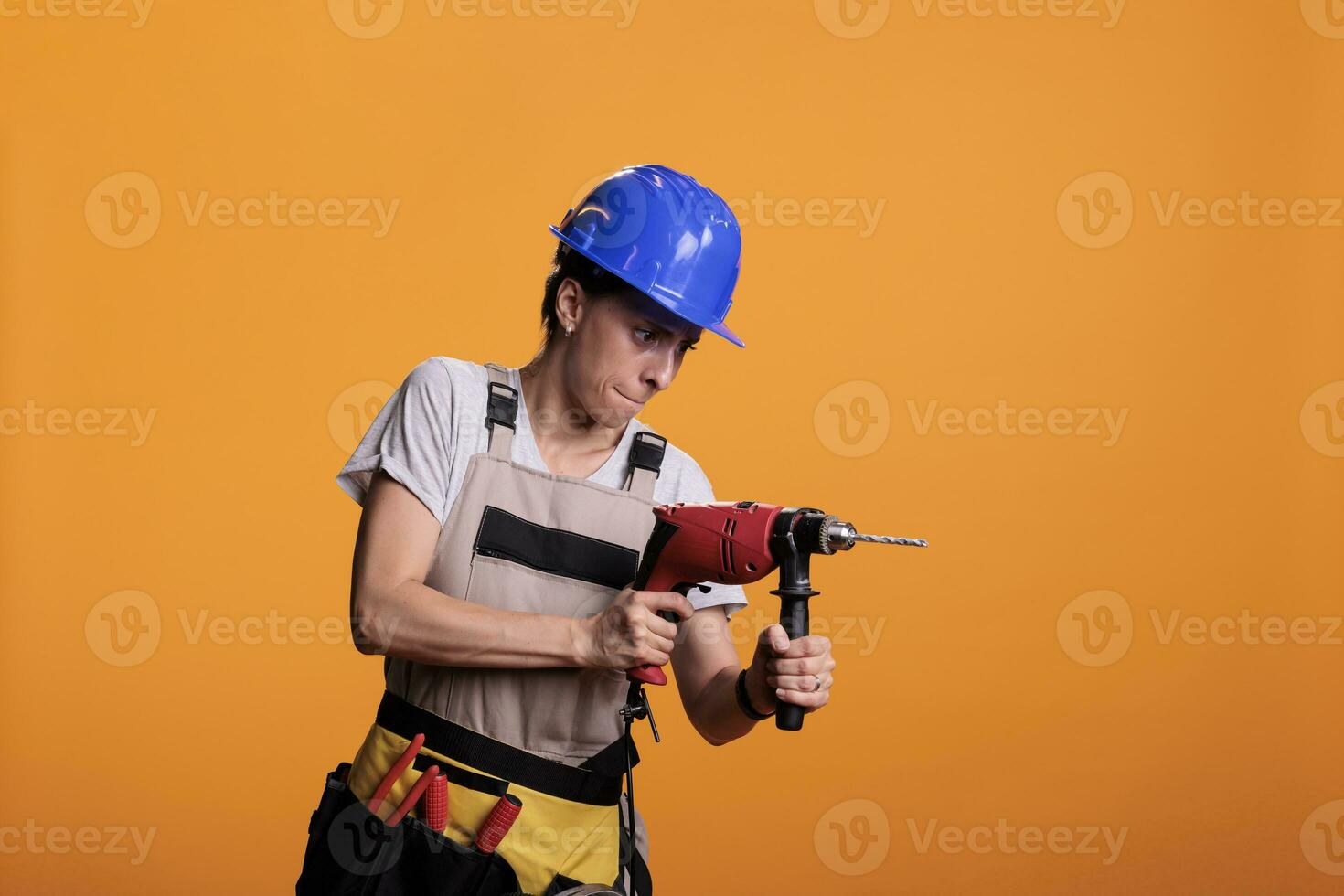 femelle industriel ingénieur en portant forage pistolet dans Nouveau intérieur rénovation projet, en utilisant Puissance percer clou pistolet. femme réparateur portant uniforme dans studio coup plus de Jaune Contexte. photo