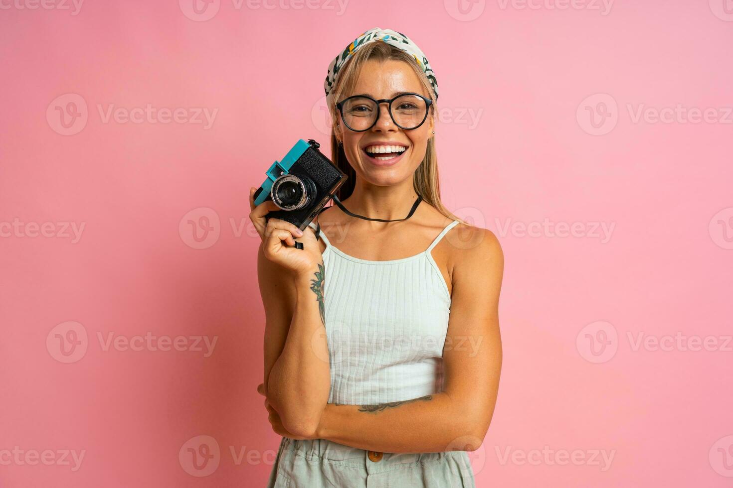 en riant blond femme en portant rétro caméra et posant sur rose Contexte. Voyage et été vacances concept. photo