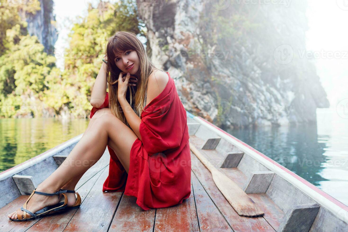 une sexy Jeune femme portant une bikini est séance sur une petit bateau près une tropical île. été vacances. photo