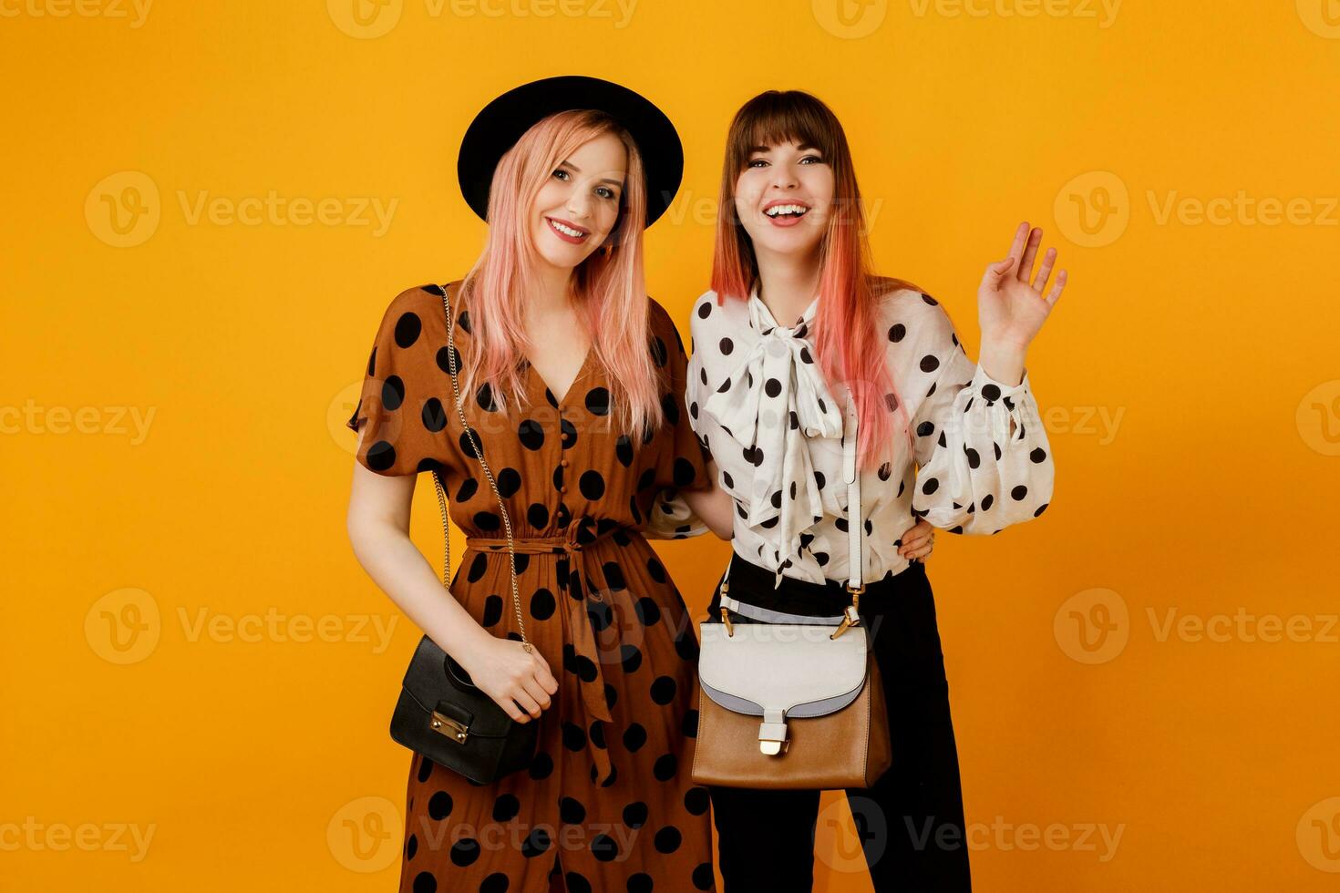 deux amis, jolie les filles en marchant et ayant amusement sur Jaune Contexte dans studio. content femme avec rose Cheveux avec sa blond ami ayant génial temps. photo