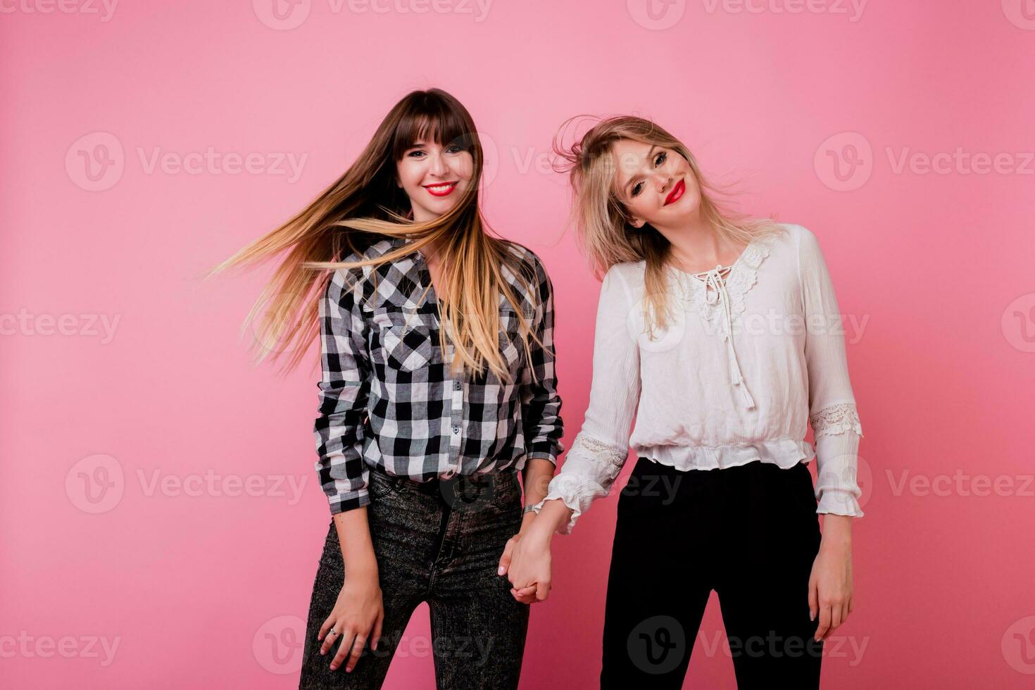 deux espiègle femmes sauter et ayant amusement dans studio sur rose Contexte. venteux Cheveux. positif ambiance. photo