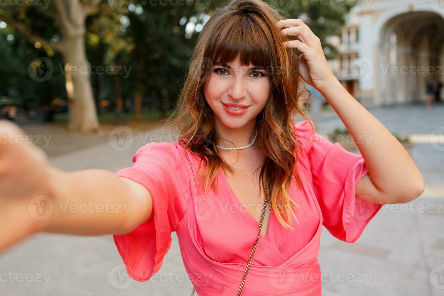 élégant femme avec parfait ondulé Cheveux fabrication soi portrait par caméra. portant rose robe. photo