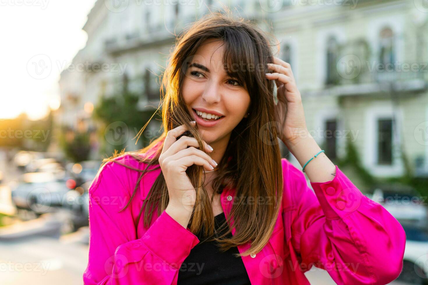 Extérieur été portrait de débonnaire bien regarder femme dans élégant rose merdique. européen rue sur Contexte. chaud le coucher du soleil couleurs. photo