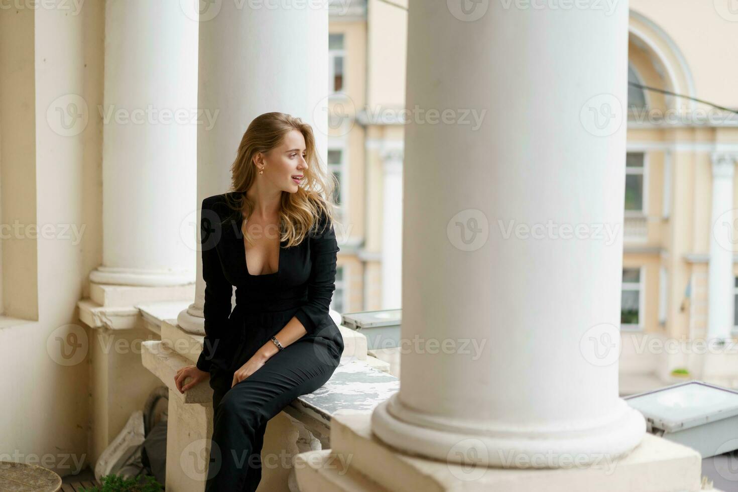 blond femme dans noir tenue posant sur terrasse. portrait de content fille je souriant et repos sur balcon. photo