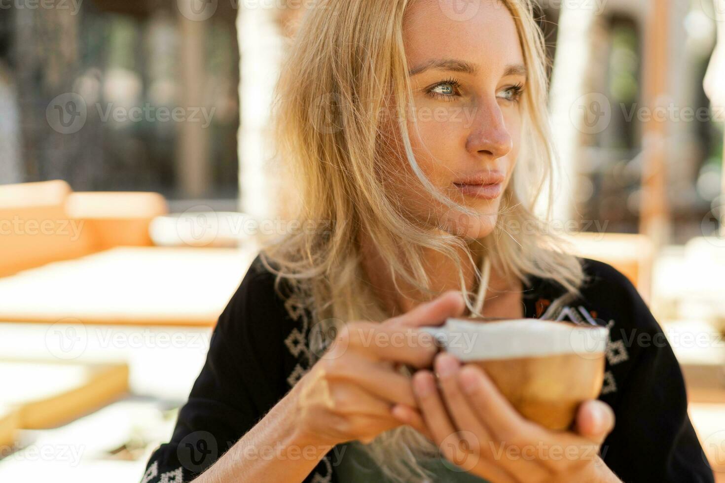 proche en haut photo de jolie blond femme enjoing vacances, effrayant dans élégant plage club. en portant tasse de café. portant élégant boho été tenue.