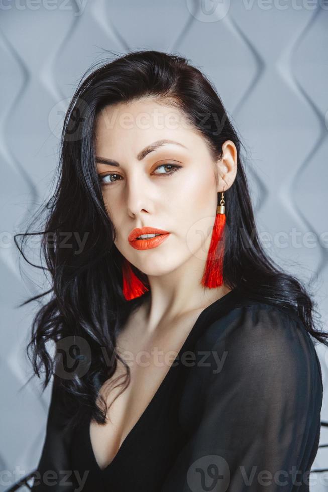 femme portant une robe noire, boucles d'oreilles rouges en studio lumineux photo