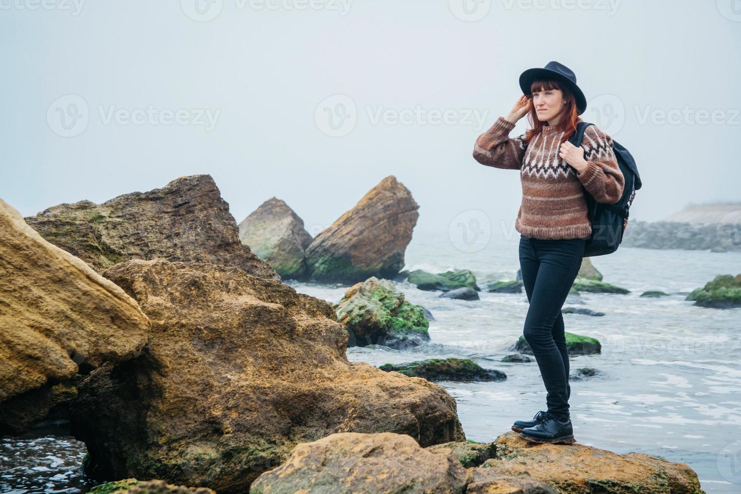 touriste femme au chapeau avec sac à dos sur les rochers sur fond de mer photo