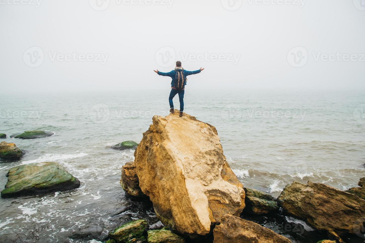 homme voyageur avec un sac à dos se dresse sur un rocher contre une mer magnifique photo