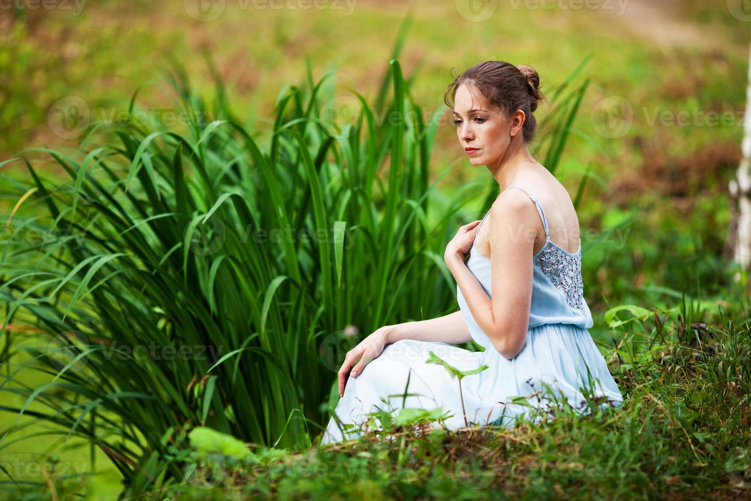 belle femme vêtue d'une robe bleue est assise sur la rive du lac photo