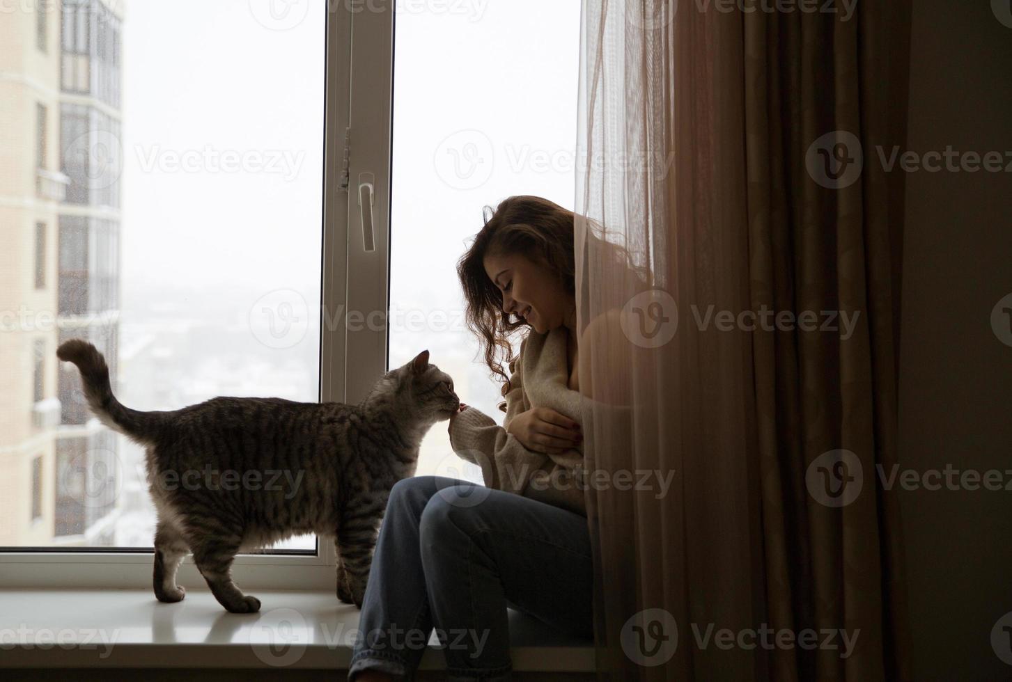 fille assise près de la fenêtre à côté d'un chat photo