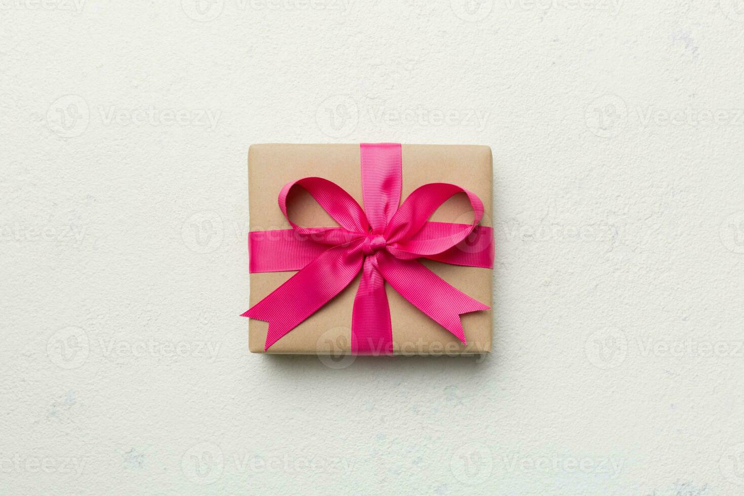 vacances cadeau boîte enveloppé dans artisanat papier avec coloré arc sur table Contexte. Haut voir, plat poser, copie espace photo