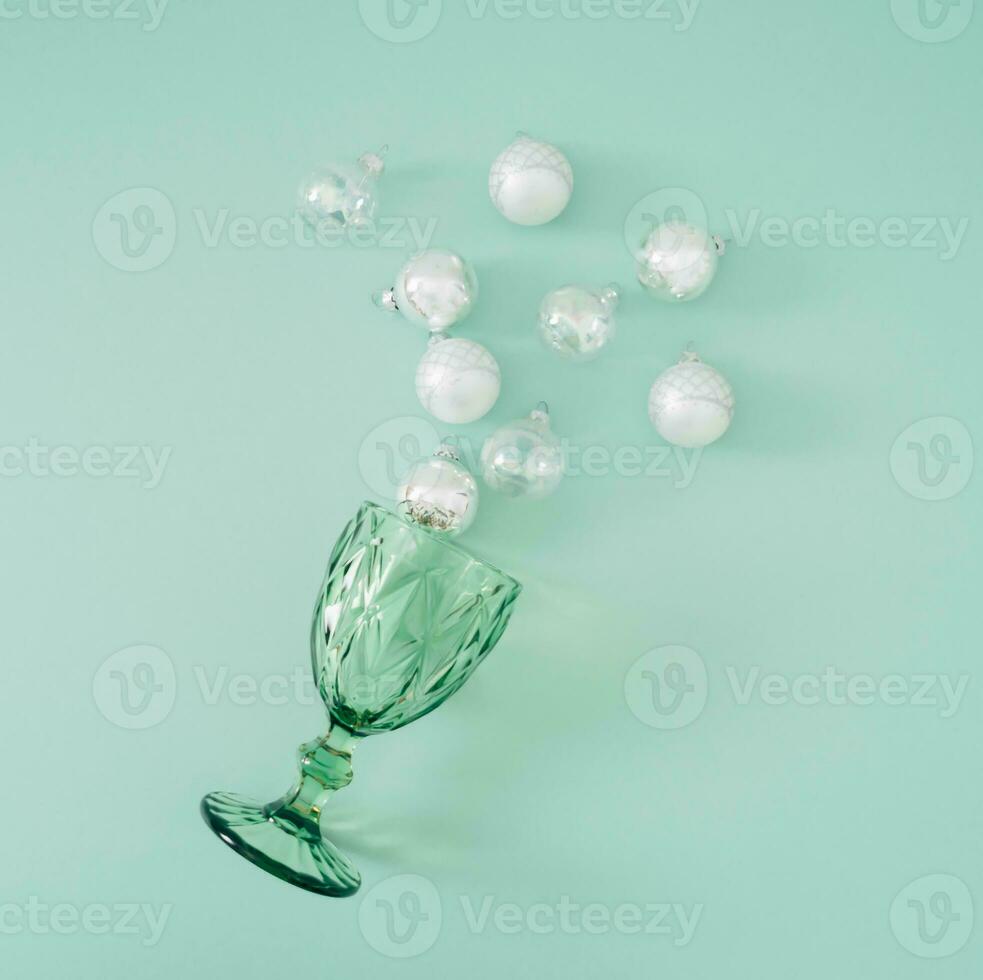 vert du vin verre avec Noël babioles décoration sur pastel vert Contexte. minimal fête concept. Créatif Noël ou Nouveau année fête idée. plat poser, Haut de voir. photo