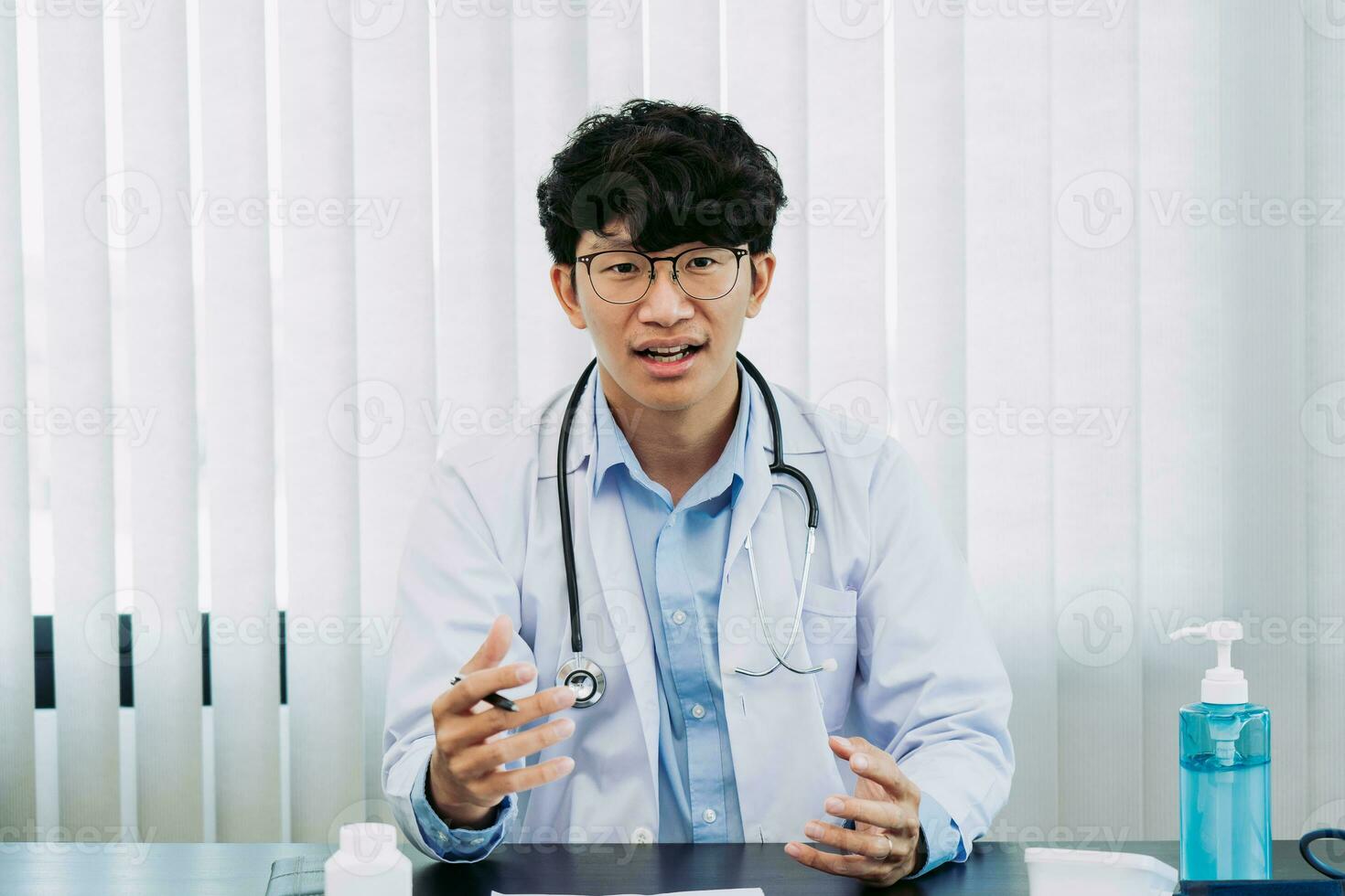 un médecin asiatique portant des lunettes et des uniformes blancs avec un stéthoscope fournit des conseils en ligne aux patients pendant l'épidémie de virus en gardant une distance sociale. photo